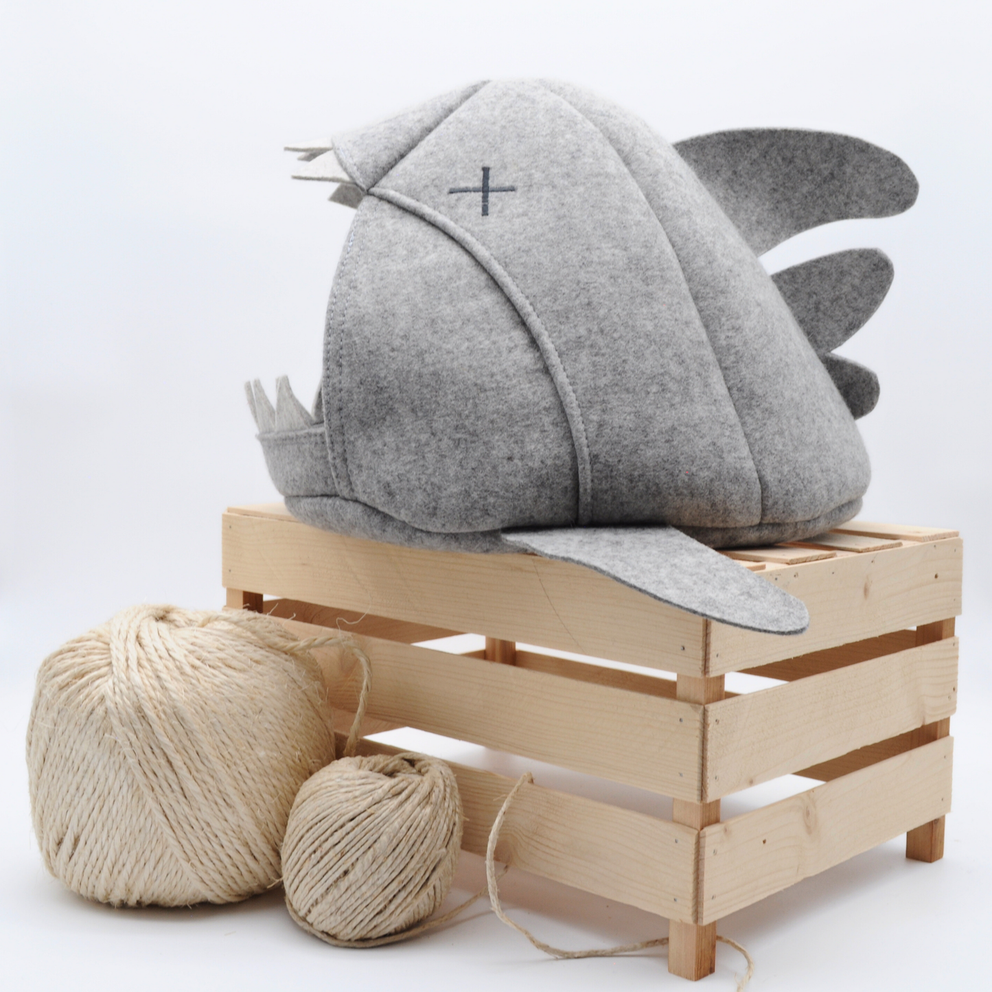 Graue Katzenhöhle in Haifischform mit gekreuzten Augen, auf Holzkiste platziert mit Sisalball im Vordergrund – natürliche Wohnatmosphäre