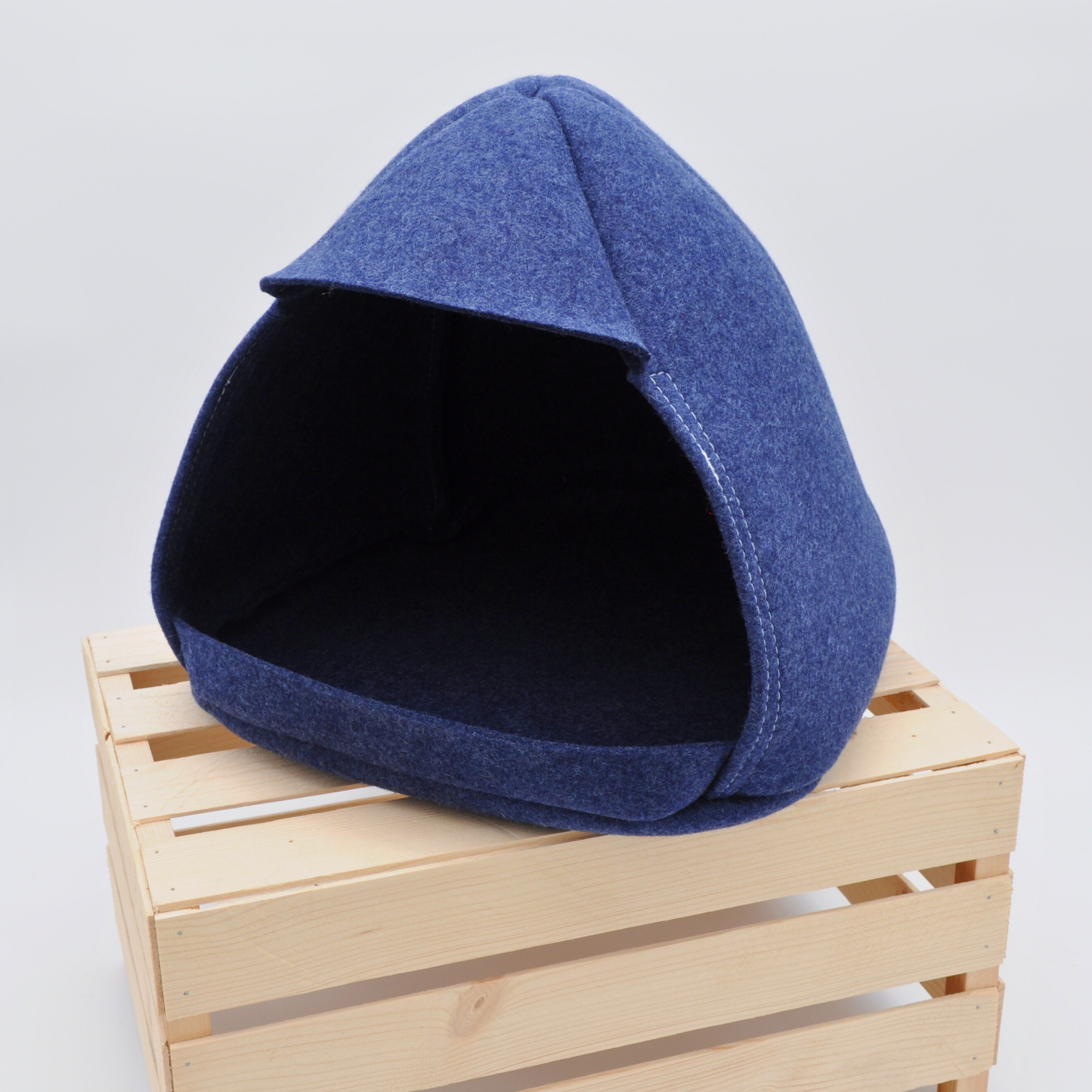 Filz-Katzenhöhle in tiefem Indigo-Blau, 45-Grad-Frontansicht auf Holzkiste