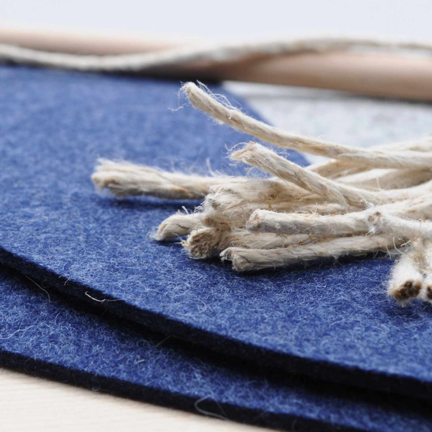 Hanfschnur-Fäden liegen auf blauem Filz, im Hintergrund verschwimmt der Holzstab der Katzenangel Wildfang