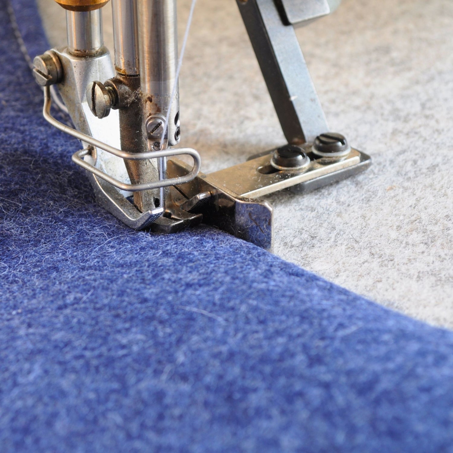 Nahaufnahme einer Nähmaschine, die blauen und grauen Wollfilz verarbeitet – Handarbeit in der Manufaktur