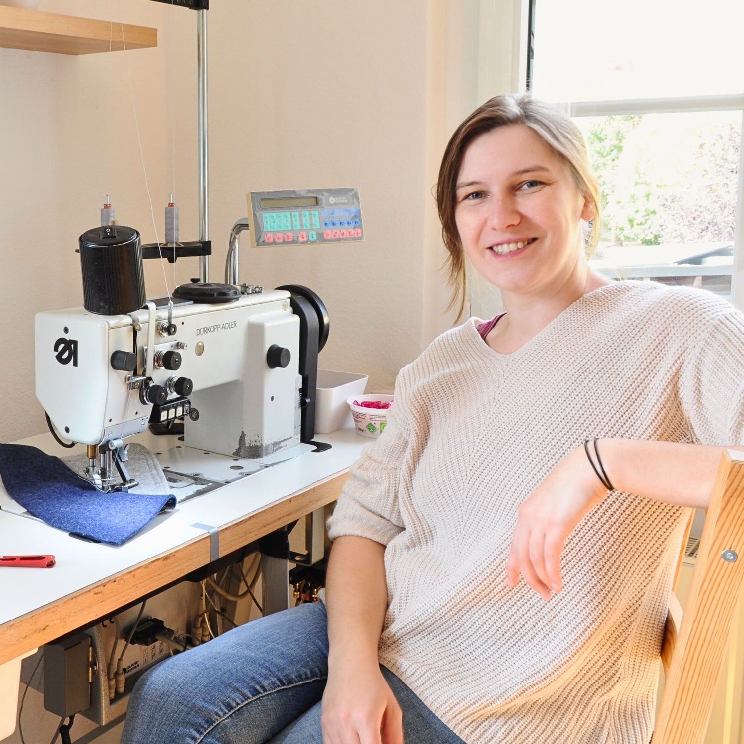 Juliane Stolz an ihrem Arbeitsplatz an der Nähmaschine, arbeitet mit Filz und lächelt in die Kamera