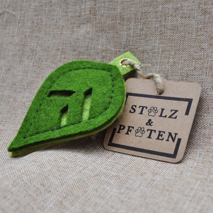 Schlüsselanhänger in Blattform aus Merino-Wollfilz mit Produktanhänger aus Karton, befestigt an einer Hanfschnur, auf beigem Leinenstoff