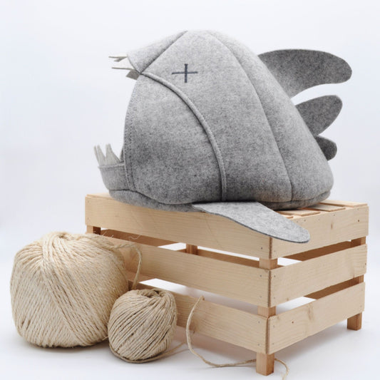 Graue Katzenhöhle in Haifischform mit gekreuzten Augen, auf Holzkiste platziert mit Sisalball im Vordergrund – natürliche Wohnatmosphäre